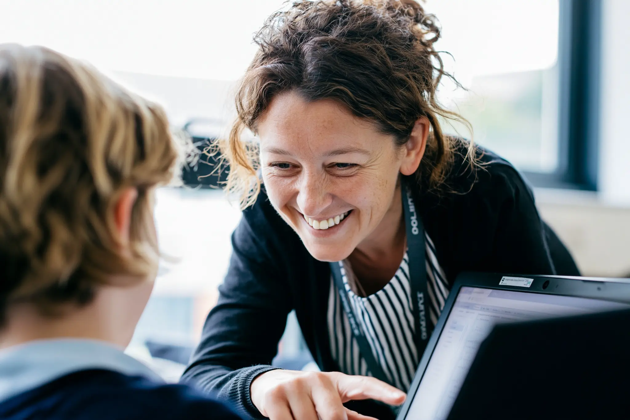 Teacher smiling while helping a pupil at a laptop