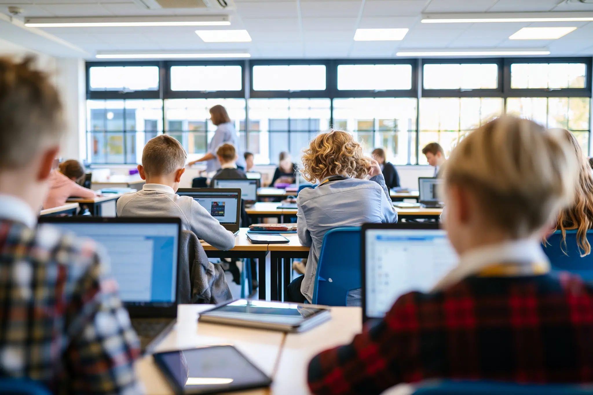 A bright classroom of pupils working on laptops with a teacher